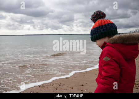 Junge zwei im roten Mantel spielen am Strand im Frühling mit Bommel hat im Alter von Stockfoto