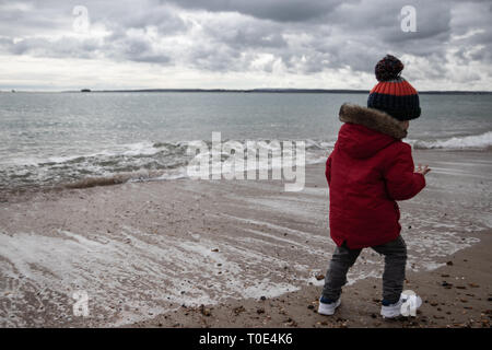 Junge zwei im roten Mantel spielen am Strand im Frühling mit Bommel hat im Alter von Stockfoto