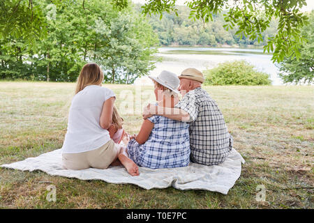 Erweiterte Familie mit drei Generationen auf einer Wiese am See im Sommer Stockfoto