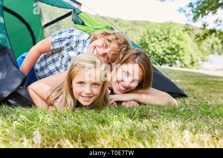 Mutter und ihre zwei Kinder sind glücklich und er liegt im Zelt auf der Wiese beim Camping Stockfoto