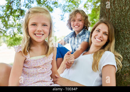 Glückliche Familie mit Mutter und zwei Kinder sitzen entspannt unter einem Stockfoto