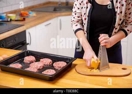 Kochen, essen und Home Konzept - Nahaufnahme der weibliche Hände reiben Käse. Kochen Fleisch Gerichte aus Hackfleisch/Faschiertem Stockfoto
