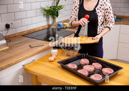 Weibliche Hand gießen mit geriebenem Käse vom Brett an der Platte. Prozess des Kochens die Koteletts oder Frikadellen. Home Kochen auf modernen Kithen Stockfoto