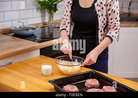 Junge Frau mischen Käse Teig mit einem Löffel in der Küche. Home Kochen von Fleisch Gericht Stockfoto