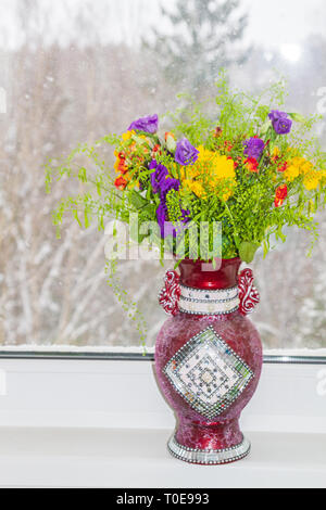 Eine schöne Vase von Frühlingsblumen steht auf ein Fenster in einem Schneesturm Stockfoto