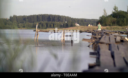 Einsame Junge sitzt auf der Kante des Pier in windigen regnerischen Wetter Stockfoto