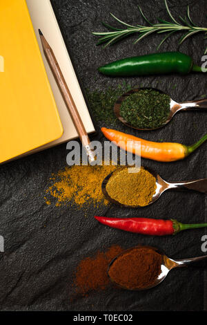 Ansicht von oben auf die Komposition Notebook für Rezept und orientalische Gewürze in Löffel und Paprika auf dem schwarz metallic Fach im asiatischen Stil Stockfoto