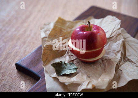 In Scheiben geschnitten roter Apfel auf natürliche Farbe Papier auf braunem Holz Schneidebrett, schneiden Zerkleinert Obst, Diät Lebensmittel Stockfoto