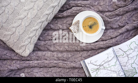 Weiße Tasse Kaffee mit Schwarm Vögel in den Himmel und Waffel Cookie in Form Tanne, weiße Seiten Buch mit Karte reisen auf Kissen und warme Wolldecke Grau karierte. Winter herbst Konzept Komfort und Träume. Stockfoto