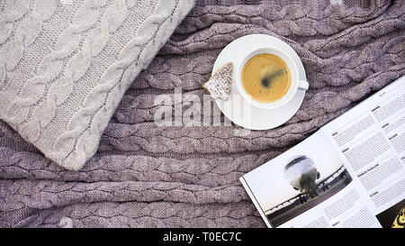Weiße Tasse Kaffee mit Cookie in Form Tanne und weiß Telefon Blume auf grau Kissen und warme Wolldecke Grau Pink Plaid. Gestrickte textile mit braid Muster. Winter herbst Komfort Stockfoto