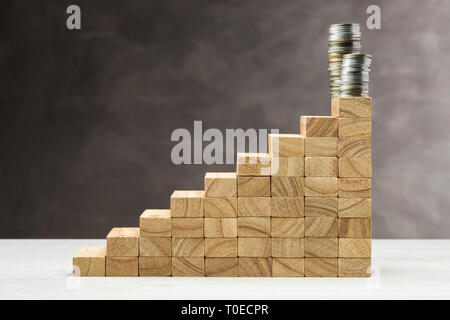 Konzept des Wachstums. Grafik mit Holzstufen auf grauem Hintergrund mit Stapel von Münzen auf. Stockfoto