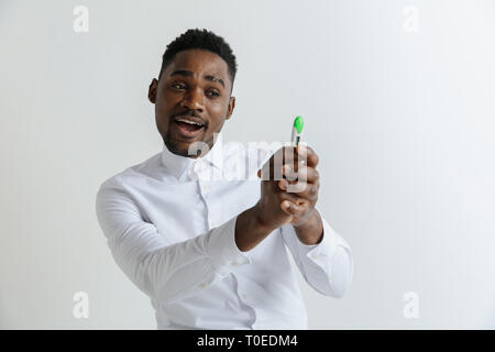 Junge glücklich afrikanische amerikanische Mann an der Schwangerschaft Test suchen. Schön lächelnde Menschen inspiriert und begeistert. Kerl gefreut, weil der Ergebnis der Schwangerschaftstest. Stockfoto