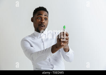 Junge glücklich afrikanische amerikanische Mann an der Schwangerschaft Test suchen. Schön lächelnde Menschen inspiriert und begeistert. Kerl gefreut, weil der Ergebnis der Schwangerschaftstest. Stockfoto