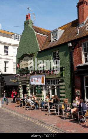 Personen außerhalb einer Kneipe in den Gassen der Küstenstadt Brighton, Sussex, England sitzen. Stockfoto