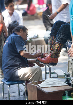 Ein Mann scheint ein Paar Stiefel mit einem Stand in der Zócalo in Oaxaca, Mexiko, 8. März 2019. Stockfoto