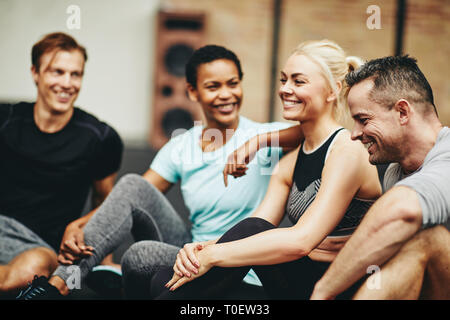 Vielfältige Gruppe von lächelnden Freunde in Sportkleidung sitzen zusammen an der Turnhalle nach dem Training Klasse Stockfoto