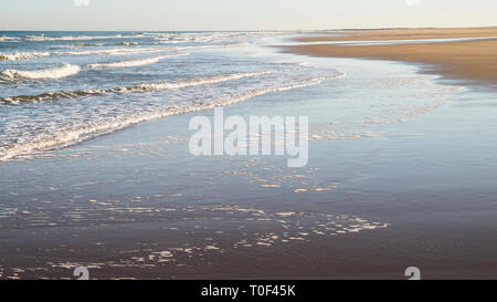 Shoreline mit Wellen am Sand an einem klaren Sonnentag auf Bamburgh, England UK. Stockfoto