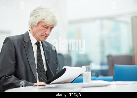 Seitenansicht Portrait von älteren Geschäftsmann holding Zwischenablage und Lesen von Dokumenten am Arbeitsplatz, im Raum kopieren Stockfoto