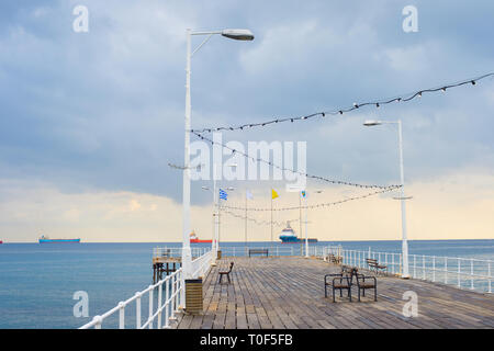 Hölzerne Seebrücke in Limassol Promenade. Indusrtial Frachtschiffe im Hintergrund. Zypern Stockfoto