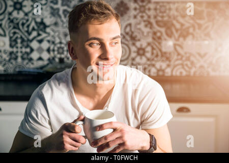 Younge blonder Mann tragen weiße T-Shirt seinen Kaffee am Morgen genießen. Stockfoto