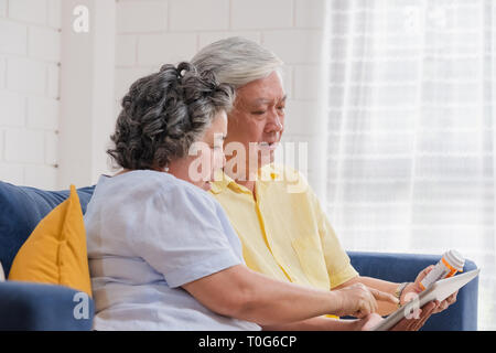 Asiatische senior Paar verwenden Tablet suche Verschreibung der Pille, während auf dem Sofa zu Hause sitzen, Senior lernen Technologie zu verwenden. Das Altern zu Hause. Stockfoto