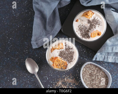 Keine gebackene Käsetorte Dessert mit zerdrückte Karotten Kekse und Chia Samen in Glas Glas auf dunklem Hintergrund. Ideen und Rezepte für gesundes Frühstück. Kopieren Sie Platz für Text. Ansicht von oben oder flach-legen. Stockfoto