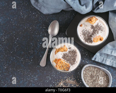 Keine gebackene Käsetorte Dessert mit zerdrückte Karotten Kekse und Chia Samen in Glas Glas auf dunklem Hintergrund. Ideen und Rezepte für gesundes Frühstück. Kopieren Sie Platz für Text. Ansicht von oben oder flach-legen. Stockfoto