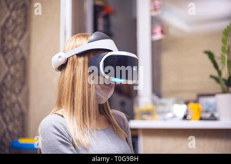 Eine junge blonde kaukasischen krankes Mädchen deckt ihr Gesicht und trägt ein Virtual Reality Headset virtual reality in ihrer Wohnung geniesst. Sie erhalten von Stockfoto