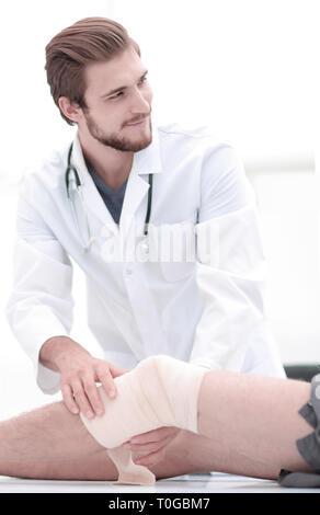 Lächelnd Arzt im Verband auf das Bein des Patienten suchen Stockfoto