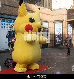 LONDON - Februar 15, 2019: ein Mann mit einem großen gelben pokemon Klage wirft mit Touristen für Geld am Leicester Square Stockfoto