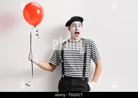 Mime-Holding ein roter Ballon und lehnte sich gegen eine Wand. Stockfoto