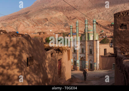 Tuyog, Turpan, China - August 12, 2012: ein Mann vorbei vor der Moschee an der Uigurischen Dorf Tuyog, mit Bergen im Hintergrund, Xinjian Stockfoto