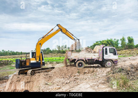 Gelber bagger Maschine laden Boden in einem Dump Truck auf der Baustelle Stockfoto