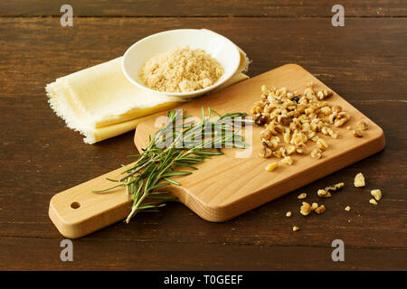 Gehackte Walnüsse mit frischen Zweige Rosmarin auf einem hölzernen Schneidebrett mit einer Schüssel mit braunem Zucker auf einem distressed Kirschholz Tisch. Stockfoto