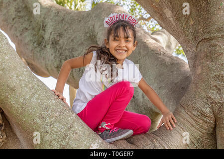 Alles Gute zum Geburtstag, das Mädchen lächelt von der Spitze des Baumes. Sie ist so aufgeregt, das oben auf einem großen Banyan Tree auf ihrem Geburtstag zu erreichen. Stockfoto