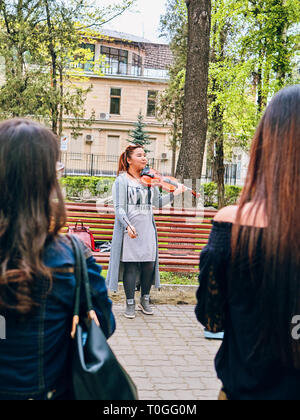 Bischkek, Kirgisistan - April 14, 2018: 2 junge Frauen zu einer Frau Künstler spielen Geige in einem Park auf der Straße hören Stockfoto