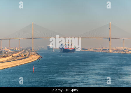 El Qantara, Ägypten - November 5, 2017: Containerschiff vorbeifahrende Schiffe Suez Kanal in den sandigen Dunst in Ägypten. Die mubarak Peace Bridge ist eine Straßenbrücke Stockfoto