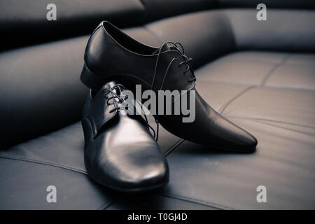 Paar elegante Marke neue schwarze Männer Schuhe auf schwarzem Leder Sofa platziert Stockfoto