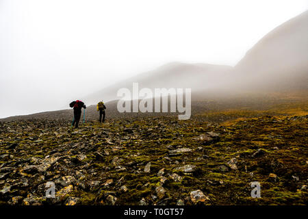 Zwei Wanderer klettern die steinigen steilen Hügel, Wolken über die Berge, Fallen in Spitzbergen, Svalbard, Norwegen hängen Stockfoto