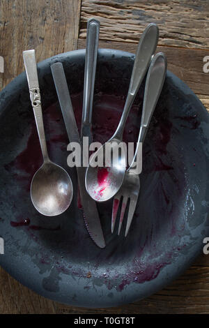 Schmutziges Besteck auf einen schmutzigen Teller mit blaubeere Soße nach einer Mahlzeit Stockfoto