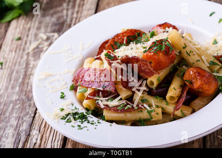 Rigatoni Nudeln mit Salami, gebratene Tomaten und Oliven, serviert köstliche italienische Gerichte mit geriebenem Parmesan auf rustikalen Holztisch Stockfoto