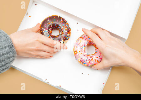 Weibliche Hände nimmt bunte Donuts. Hände greifen zwei letzten Donuts im pastellfarbenen Hintergrund. Stockfoto