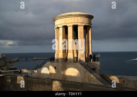 Belagerung Bell War Memorial in schönen sunste Licht, Valetta, Malta, Meer, die Mauer der Festung, Brücke über das Meer, wirbelnde Wolken im Himmel. Stockfoto