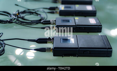 Vier drahtlose Mikrofon, Sender und vier drahtlose Mikrofon Empfänger auf Glas Tisch im TV-Studio Stockfoto