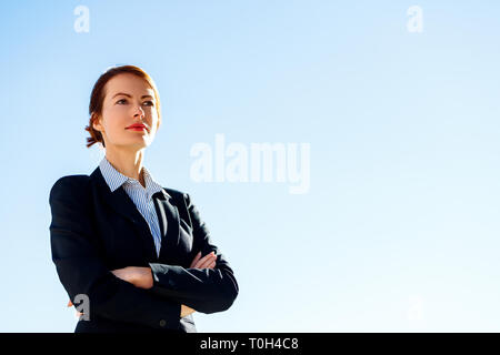 Business Frau mit gekreuzten Händen steht gegen den klaren blauen Himmel. Stockfoto