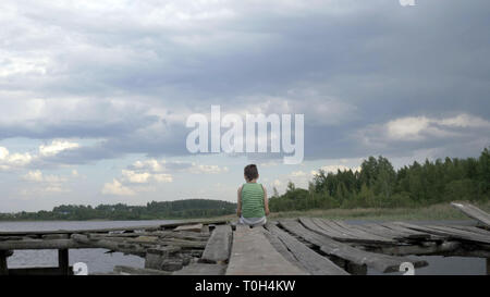 Einsame Junge sitzt auf der Kante des Pier in windigen regnerischen Wetter, Spaß haben Stockfoto