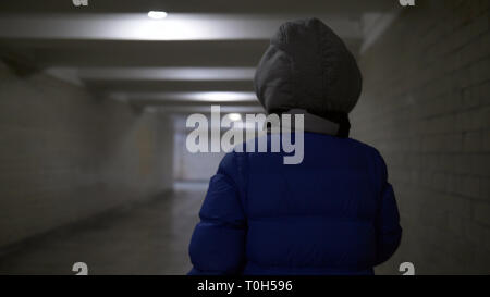 Teenager boy Spaziergänge durch einen schmalen dunklen Tunnel im Winter, etwas in seiner Hand hält, Rückansicht Stockfoto