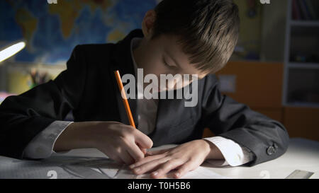 Junge Hausaufgaben zu Hause am Abend, sitzt am Tisch in einer Jacke Stockfoto