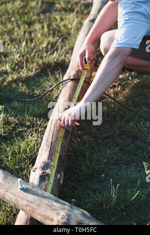 Mann mit Stahl Maßband zum Messen von Holz bei der Arbeit im Garten Stockfoto