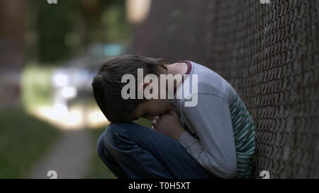 Geschmerzt traurige einsame Junge sitzt auf dem Boden, auf der Natur in tiefe Depression, niemand wartet auf den Jungen zu Hause Stockfoto